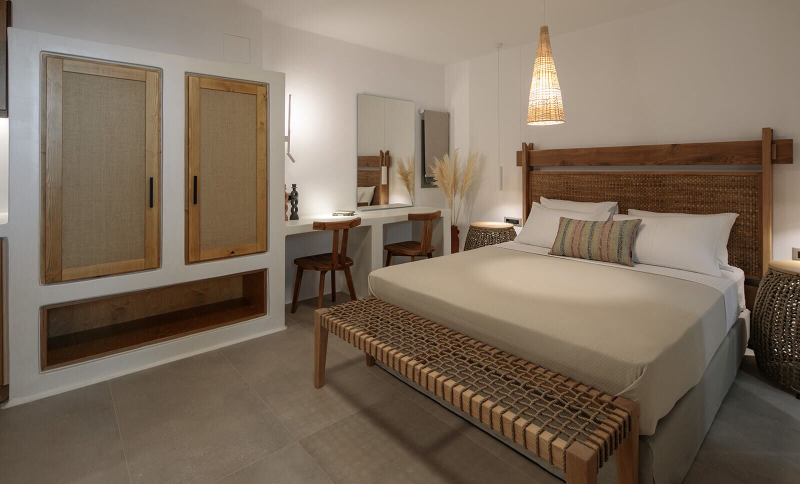 A bedroom with a large bed, wooden wardrobe, desk, and a hanging light fixture.