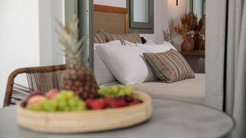 Een kamer met een bed, een rieten stoel en een tafel met een fruitschaal.