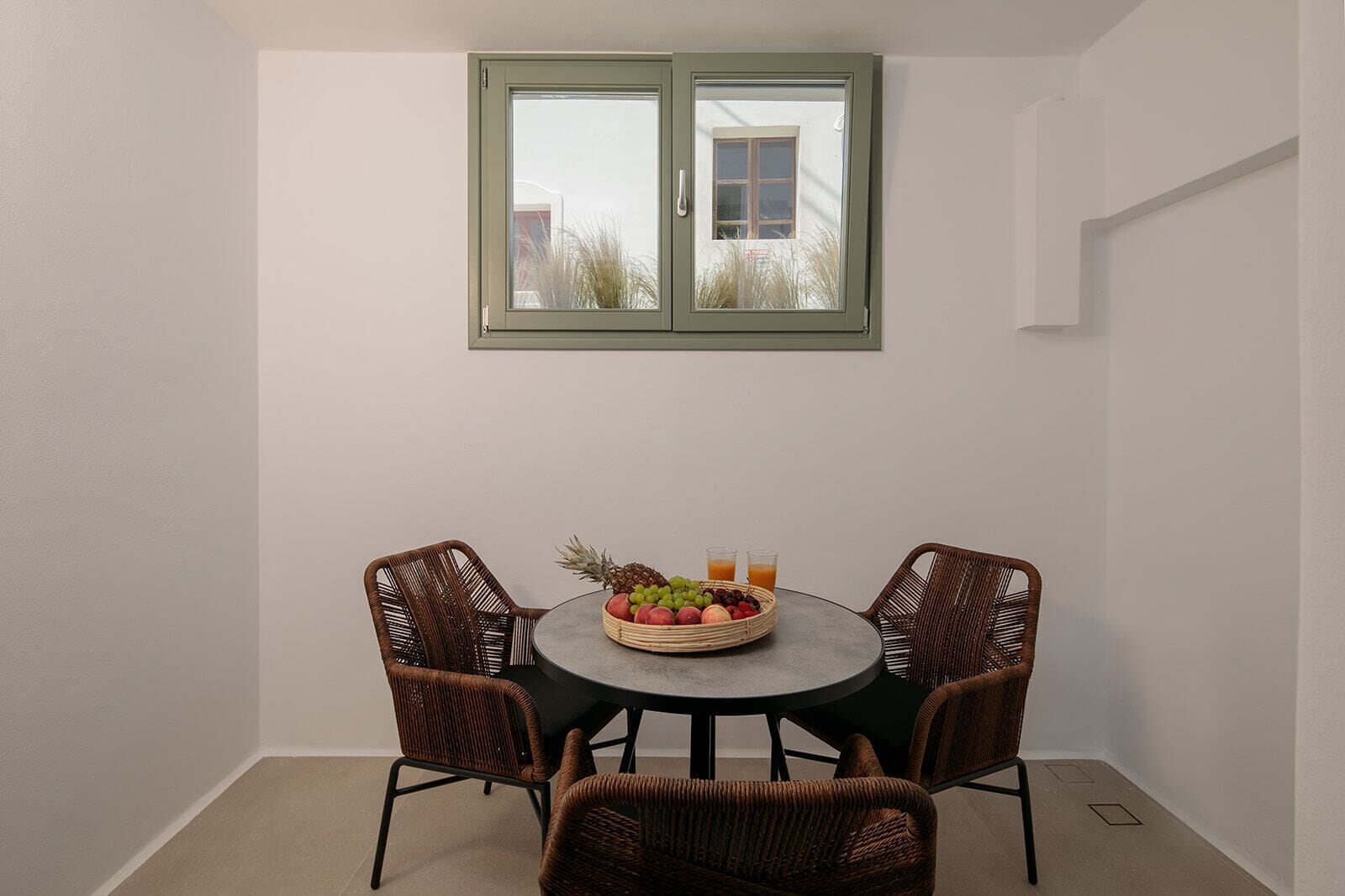 A small dining area with a round table and four wicker chairs, a fruit basket, and two glasses of orange juice on the table.