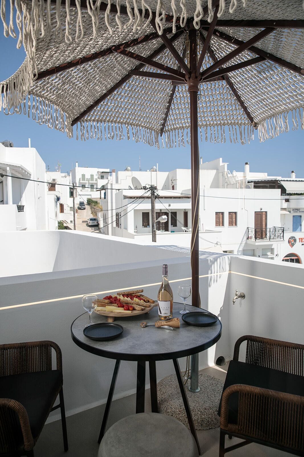 A terrace with a table set for two, a bottle of wine, and a plate of food.