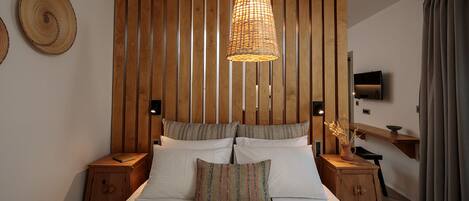 Un dormitorio con cabecera de listones de madera, una cama grande con muchos cojines, mesitas de noche, un televisor y un pequeño armario de madera.