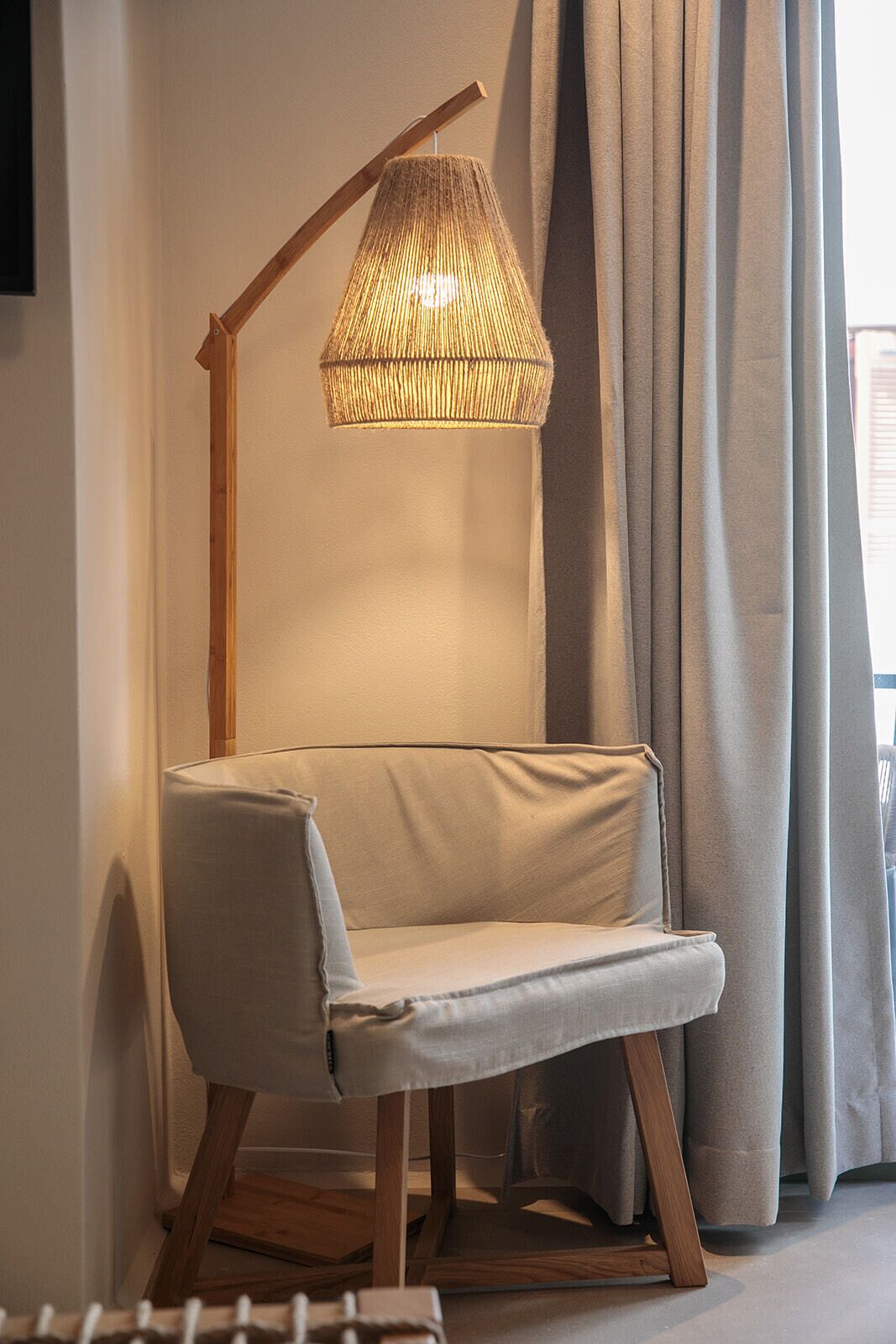 A modern room with a wooden floor lamp, a cushioned bench, and a window with curtains.