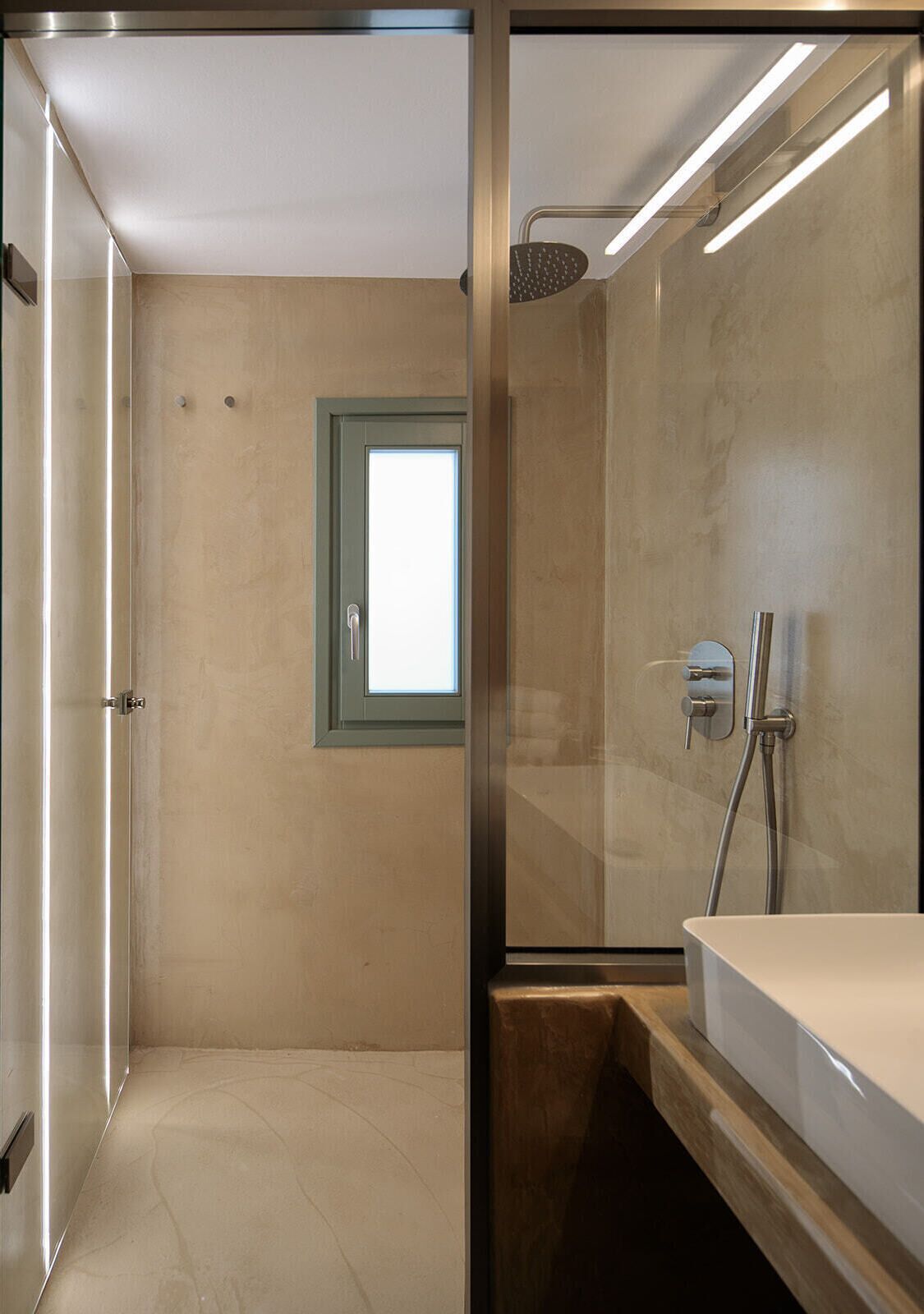 A modern bathroom with a glass shower enclosure, a built-in sink, and a small window.