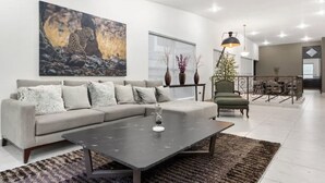Un salon moderne avec un canapé gris, une table basse noire et une grande œuvre d’art à motifs léopard accrochée au mur.