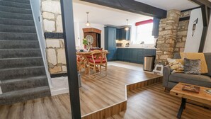 En moderne stue med trappe, spiseplads og køkken med blå skabe samt en væg med stenudsmykning.