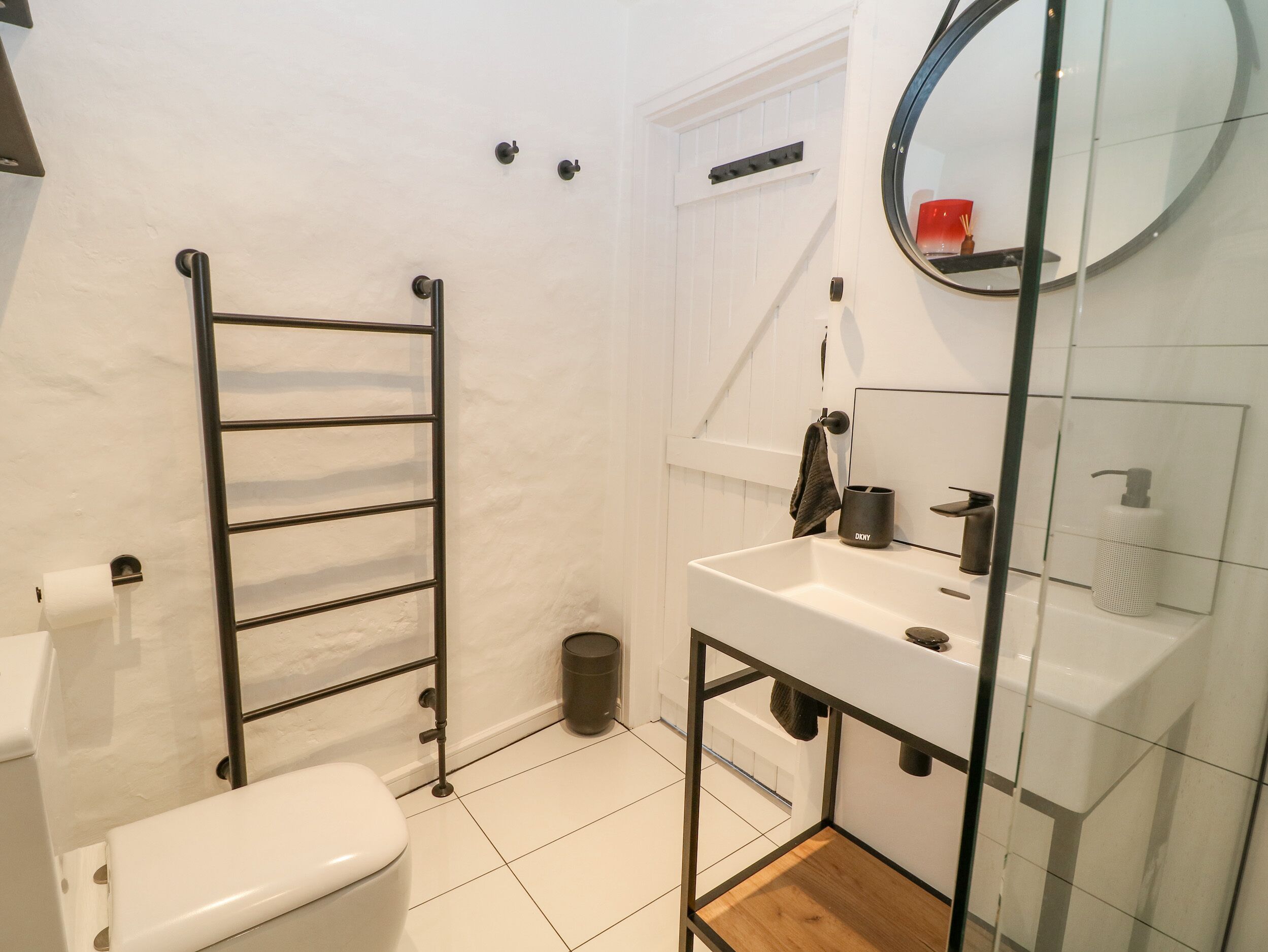 A bathroom with a toilet, a towel rack, a sink, a mirror, and a trash bin.