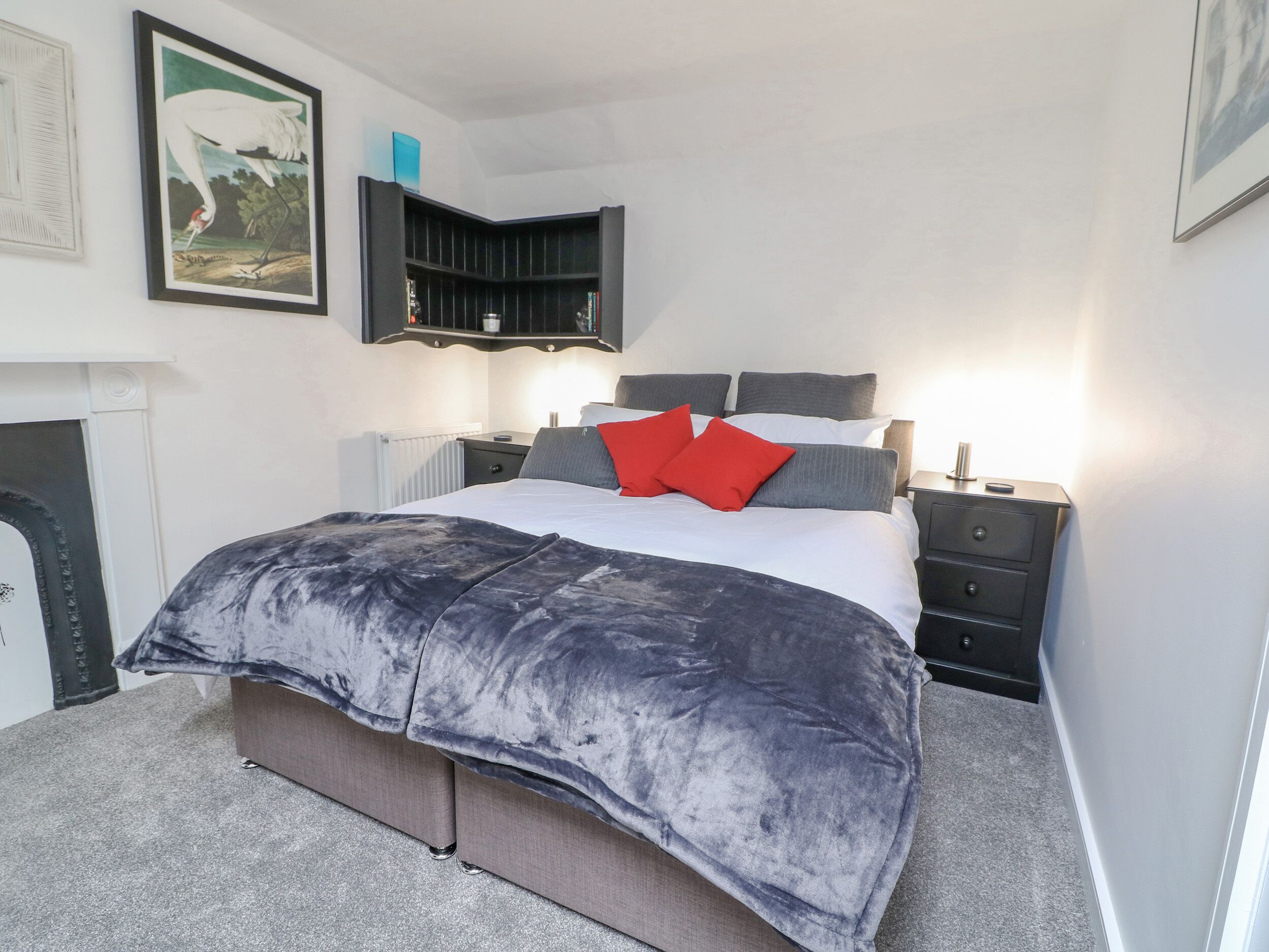 Ein modernes Schlafzimmer mit einem großen Bett, grau und roten Kissen, einem dunklen Kopfteil, Nachttischen und einer schwarzen Regaleinheit.