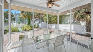 A covered patio with a ceiling fan, white chairs, and a glass table.