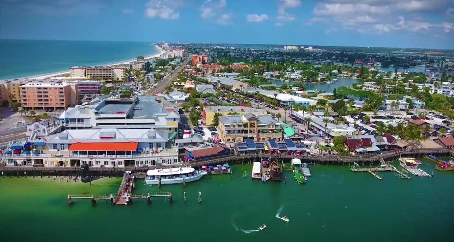 An aerial view of a coastal town with a marina, buildings, and a beach.