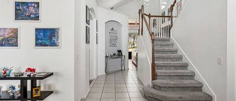 A hallway with a staircase, tiled floor, and artwork on the walls.