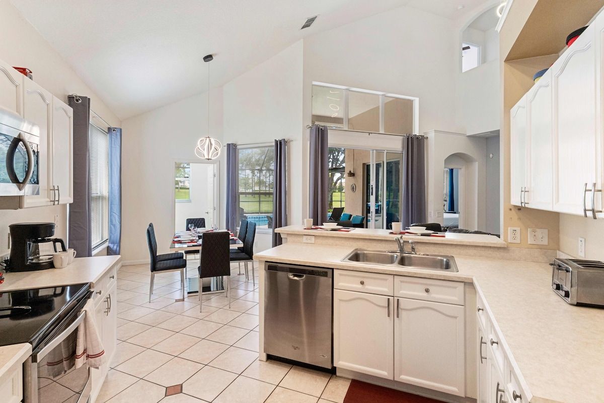 A modern kitchen with white cabinetry, a dishwasher, and a dining area with a table and chairs.