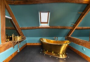 Relax in a room with a sloped ceiling, wooden beams, and a bathtub.