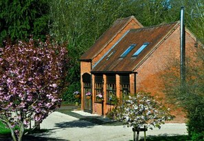 Standalone building with a pitched roof and a small porch area, surrounded by lush greenery and flowering trees.
