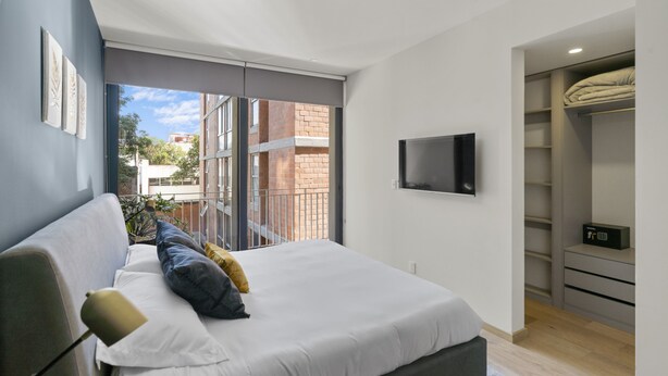 Un dormitorio moderno con una cama grande, un televisor montado en la pared y una puerta corrediza de vidrio que da a un espacio exterior.