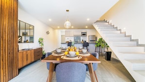 Un comedor moderno con una mesa de madera, sillas tapizadas en gris y una escalera que conduce a un nivel superior.