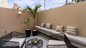 Una terraza en la azotea con un sofá, dos sillones, una mesita redonda con una bandeja de cruasanes y una planta en maceta.