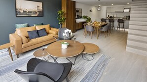 Una sala moderna con sofá, mesa de centro y sillas, un comedor con mesa y sillas, y una cocina al fondo.