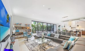 A modern living room with a sofa, coffee table, and a TV. There is a dining area with chairs and a table.