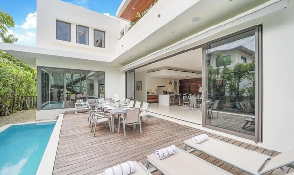 A modern house with a pool, outdoor dining area, and large sliding glass doors leading to a kitchen.