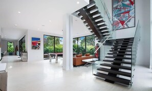 A modern interior with a glass staircase, a dining area, and large windows.