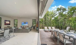 A modern living room with a TV, seating, and a view of lush greenery.