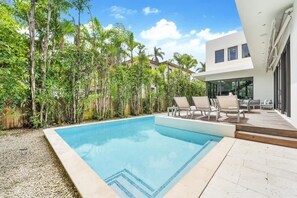 Ein rechteckiger Pool mit Fliesenrand, umgeben von einer Liegefläche mit Liegestühlen.