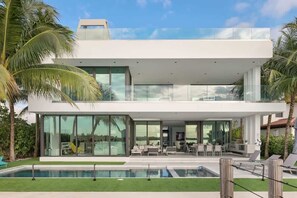 A modern two-story house with a swimming pool, large glass windows, and outdoor seating. - Luxury Bayfront Villa with Heated Pool & Hot tub (North Bay Village)
