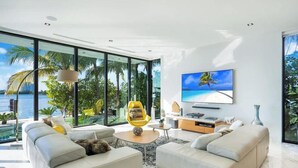 Ett modernt vardagsrum med en stor TV, bekväma sittmöbler och utsikt över havet.
