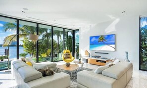 A modern living room with a large TV, comfortable seating, and a view of the ocean. - Luxury Bayfront Villa with Heated Pool & Hot tub (North Bay Village)