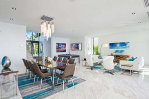 A modern living room with a dining area, a pool table, and a staircase leading to an upper level. - Luxury Bayfront Villa with Heated Pool & Hot tub (North Bay Village)