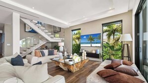 Un saló modern amb una escala, una finestra gran amb vista a la platja i una taula de cafè amb objectes decoratius.