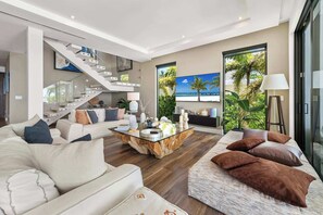 A modern living room with a staircase, a large window with a beach view, and a coffee table with decorative items.