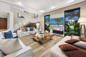 A modern living room with a staircase, a coffee table, and a large window with a view of palm trees.