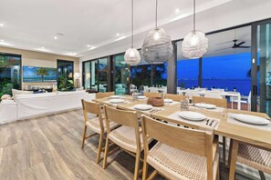 A modern dining area with a view of the ocean, large windows, and a ceiling fan.