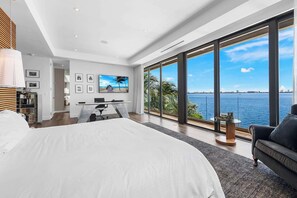 A modern bedroom with a large bed, a desk, and a view of the sea. - Luxury Bayfront Villa with Pool New Construction (North Bay Village)