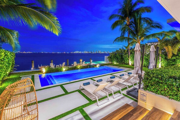 A pool area with lounge chairs and a view of the city skyline at night.