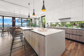 A modern kitchen with a large island, wooden cabinets, and pendant lighting.