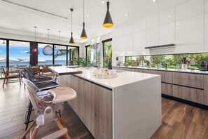 A modern kitchen with a large island, bar stools, and a view of the sea. - Luxury Bayfront Villa with Pool New Construction (North Bay Village)