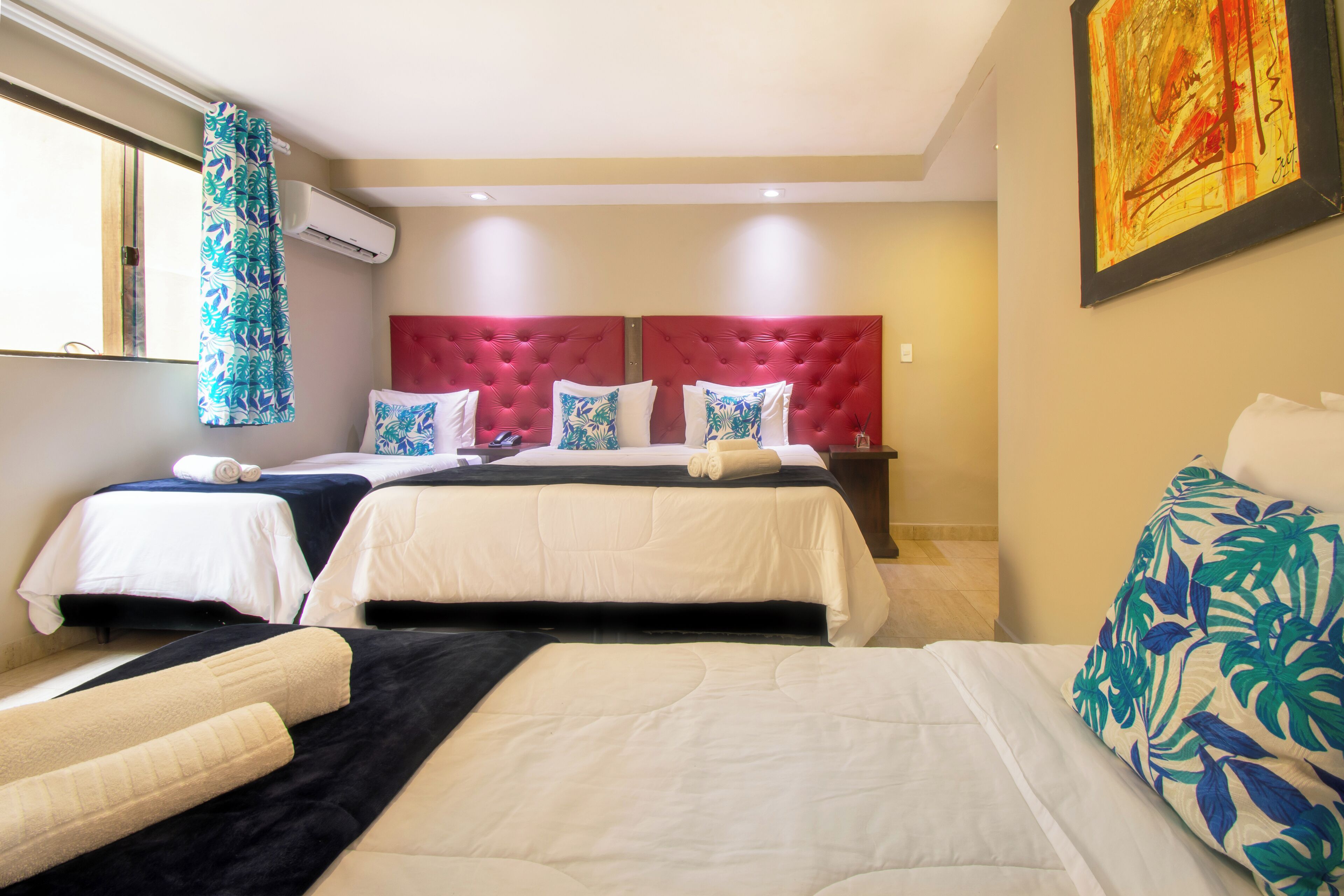 A hotel room with two beds, a large window with curtains, an air conditioning unit, and a painting on the wall.