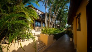 A narrow pathway leading to a building with a tiled roof, surrounded by lush greenery and potted plants. - Hotel Barra da Lagoa by Latitud Hoteles (Búzios)
