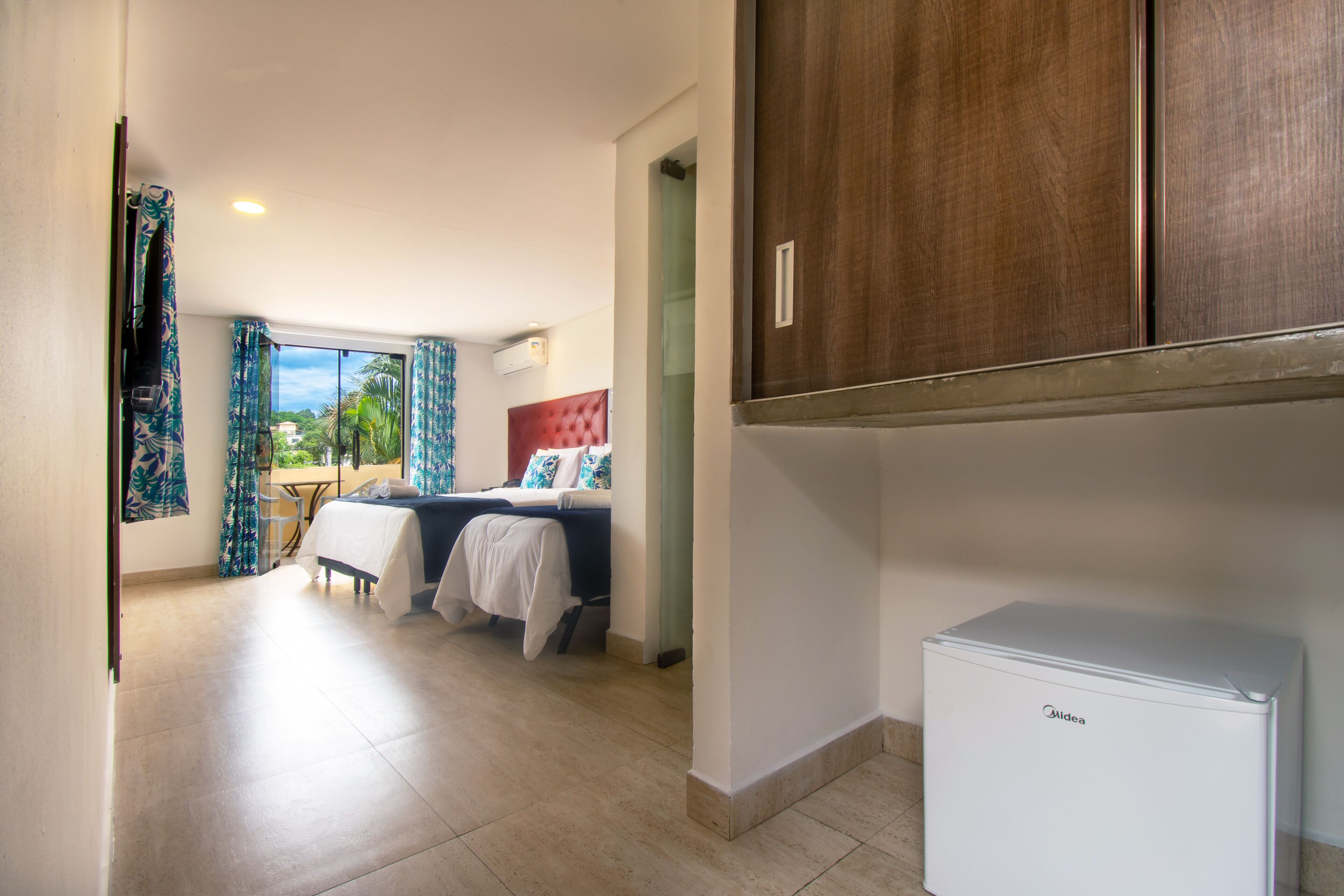 A hotel room with a bed, a small table, a refrigerator, and a view of the outdoors.