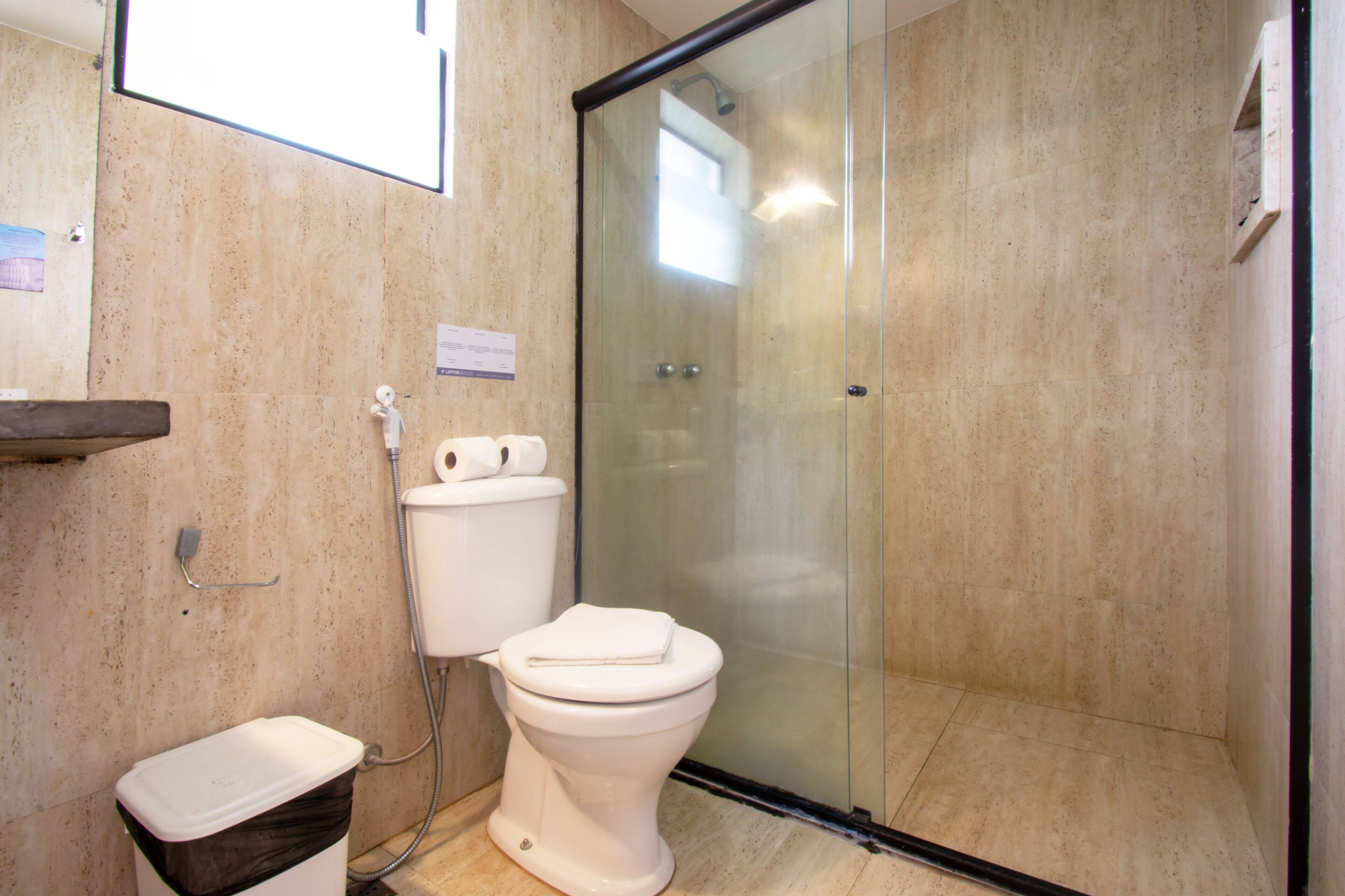 A modern bathroom with a glass-enclosed shower, a toilet, and a trash bin.