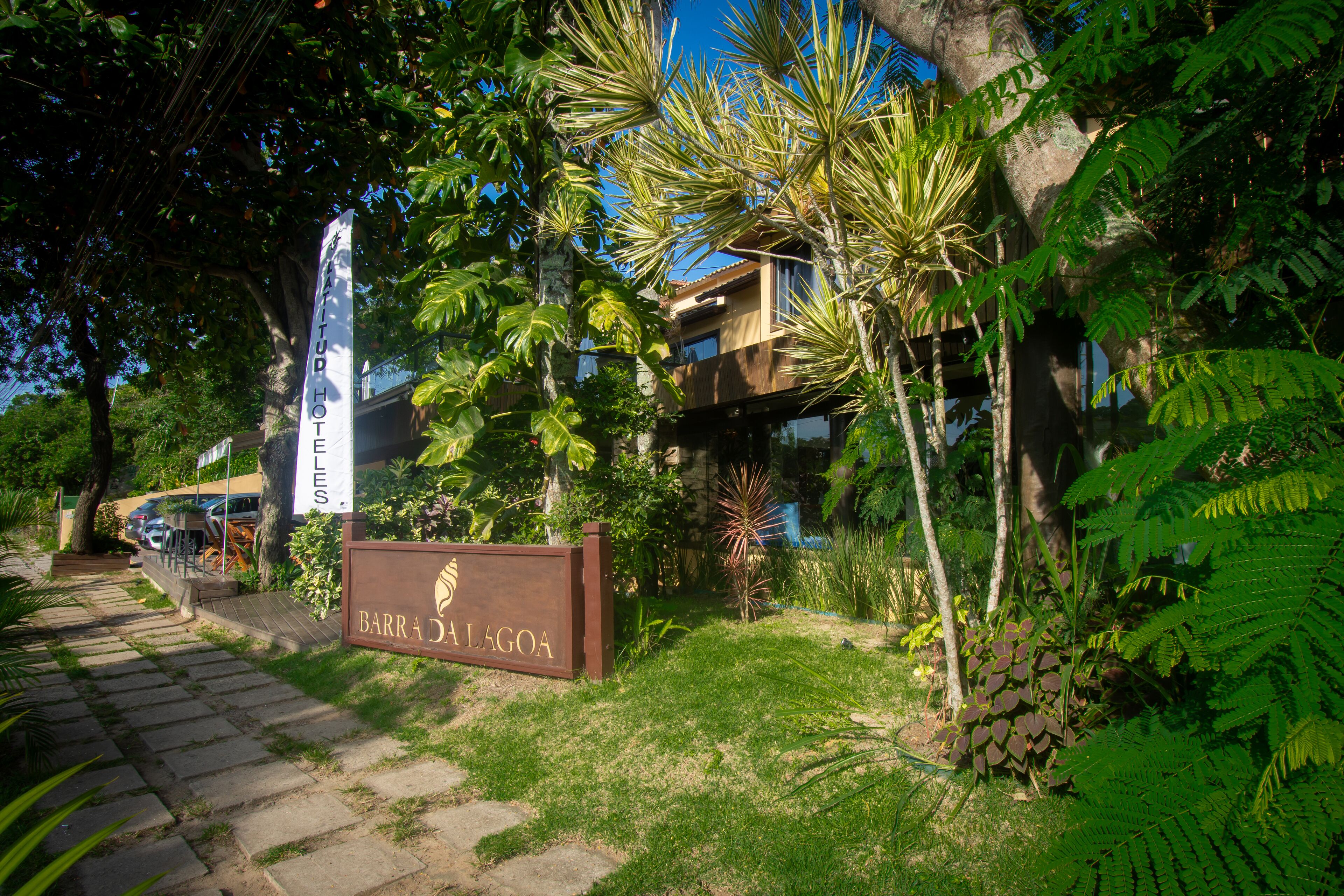 A hotel entrance with a sign reading "Barrada Lagoa" surrounded by lush greenery and a clear sky.