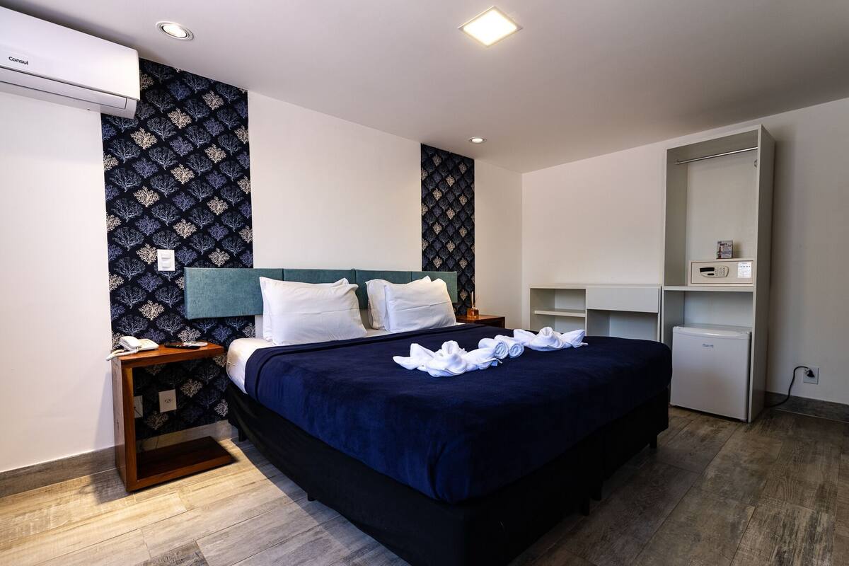 Une chambre d’hôtel équipée d’un lit, d’une table de chevet, d’un climatiseur et d’un petit réfrigérateur.