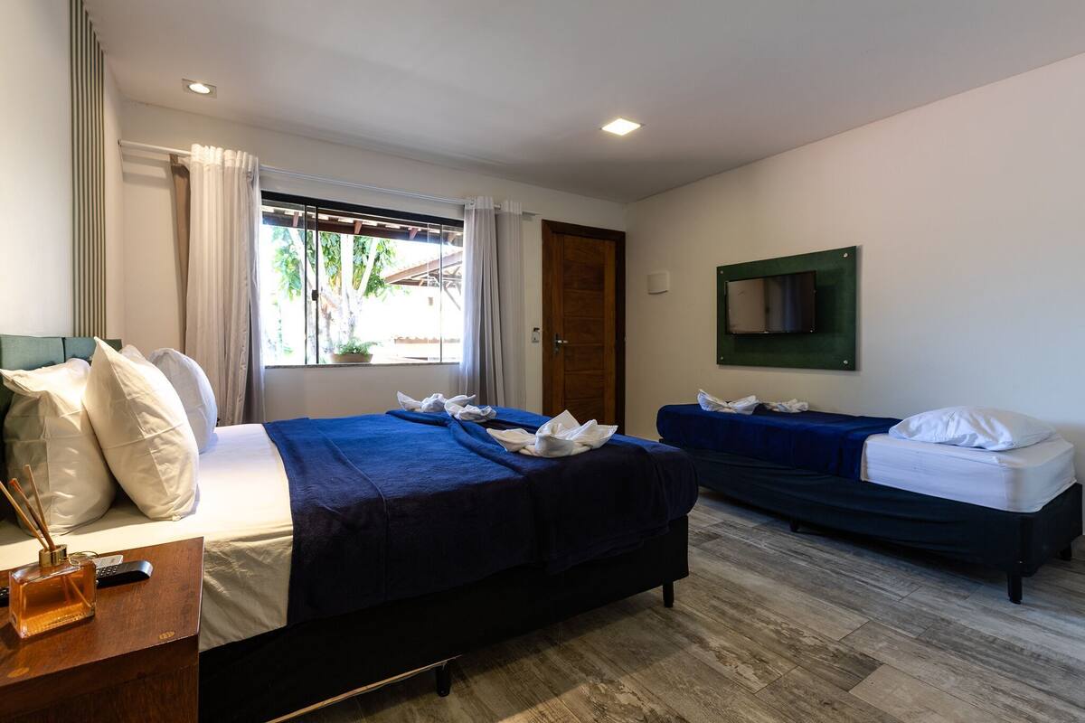 Une chambre d’hôtel avec deux lits, une commode en bois, une télévision et une fenêtre avec des rideaux.