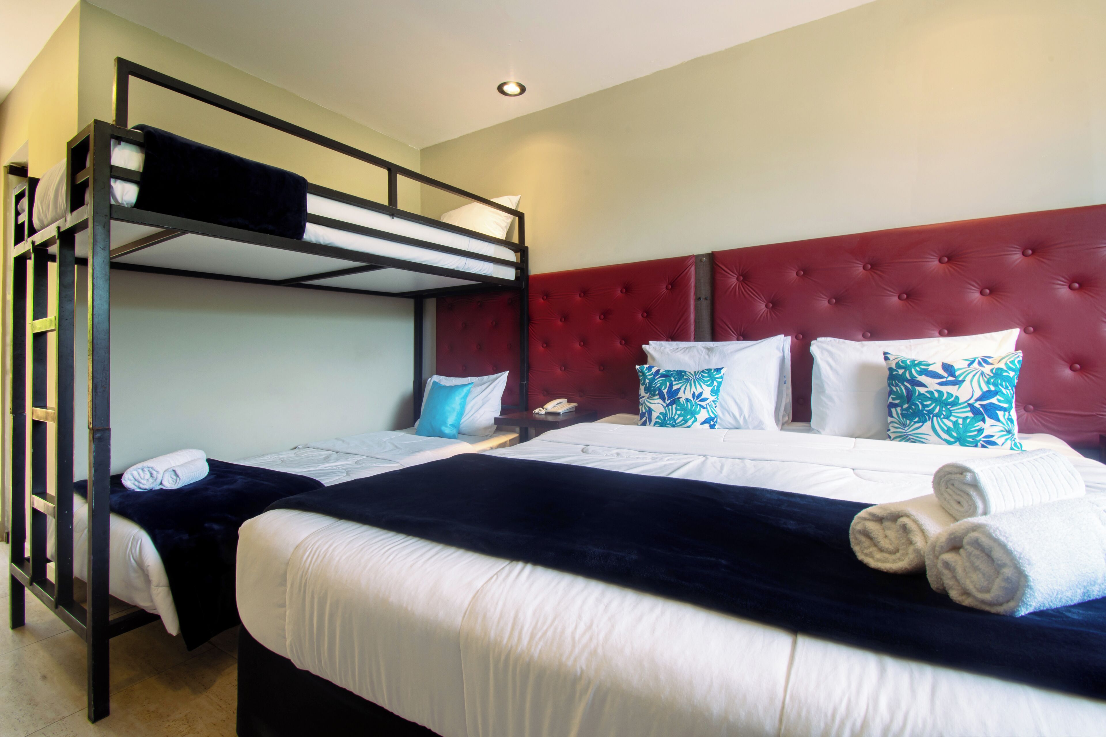 A hotel room with bunk beds, a red upholstered headboard, and neatly made beds with towels.