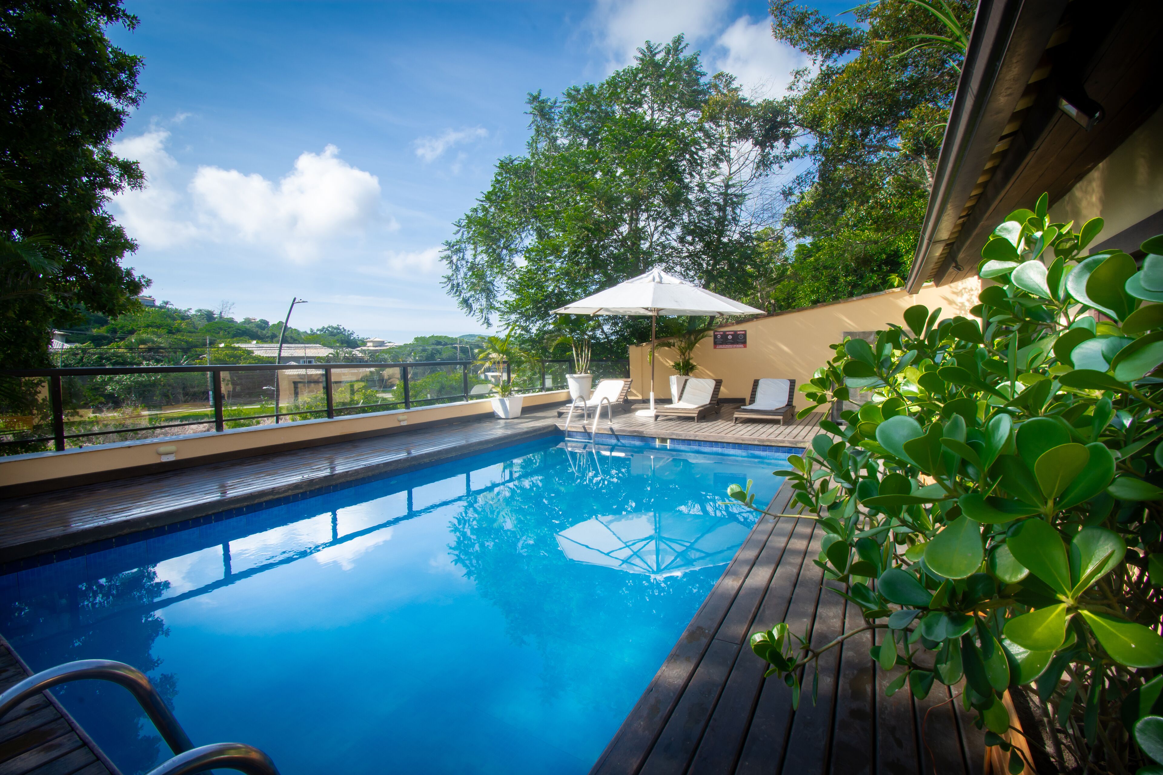 A swimming pool with lounge chairs and a sun umbrella, surrounded by greenery and a clear sky.
