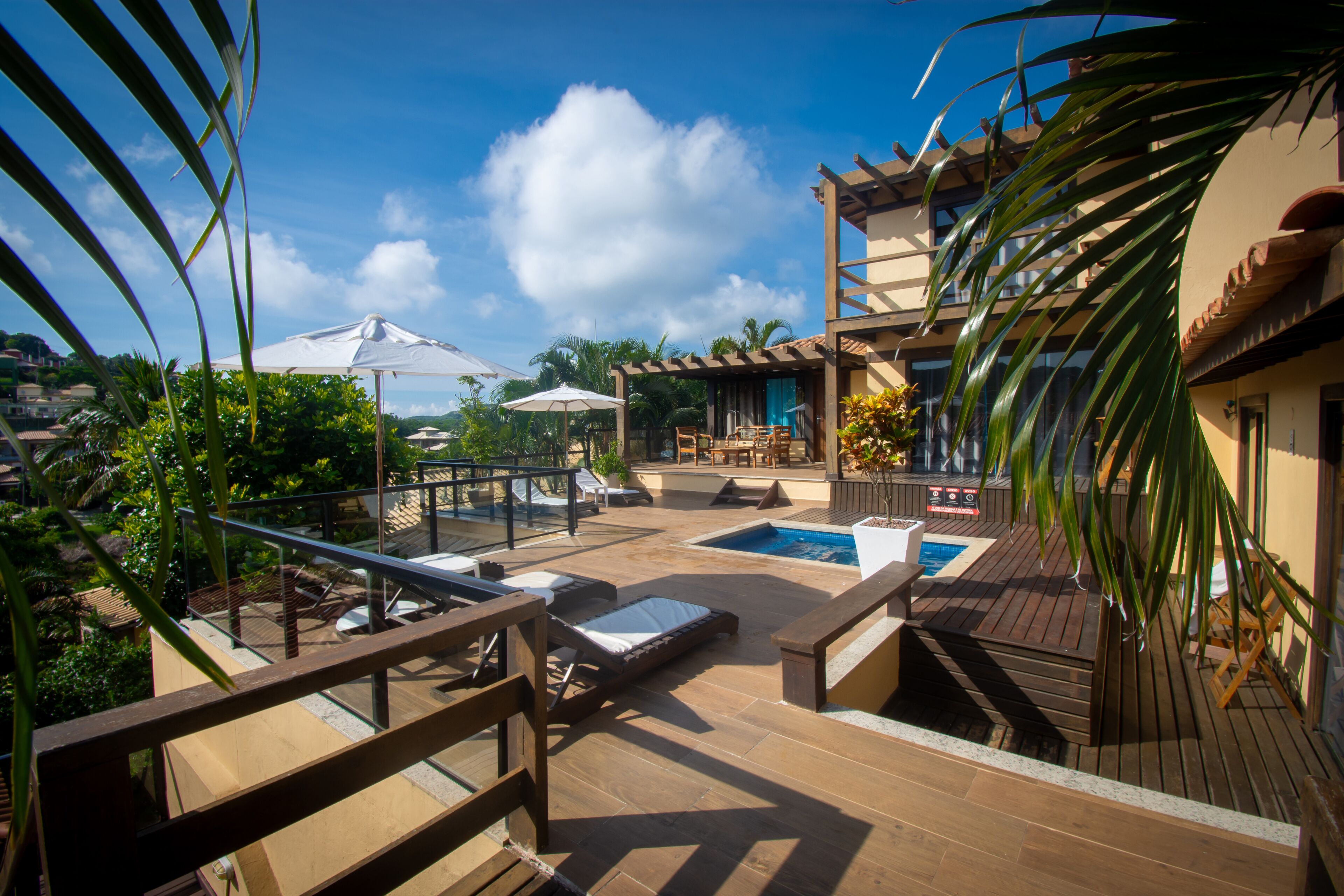 A rooftop pool area with lounge chairs, umbrellas, and a wooden deck.