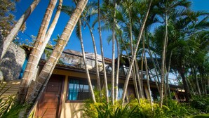 A tropical resort with palm trees, a stone wall, and a wooden door. - Hotel Barra da Lagoa by Latitud Hoteles (Búzios)