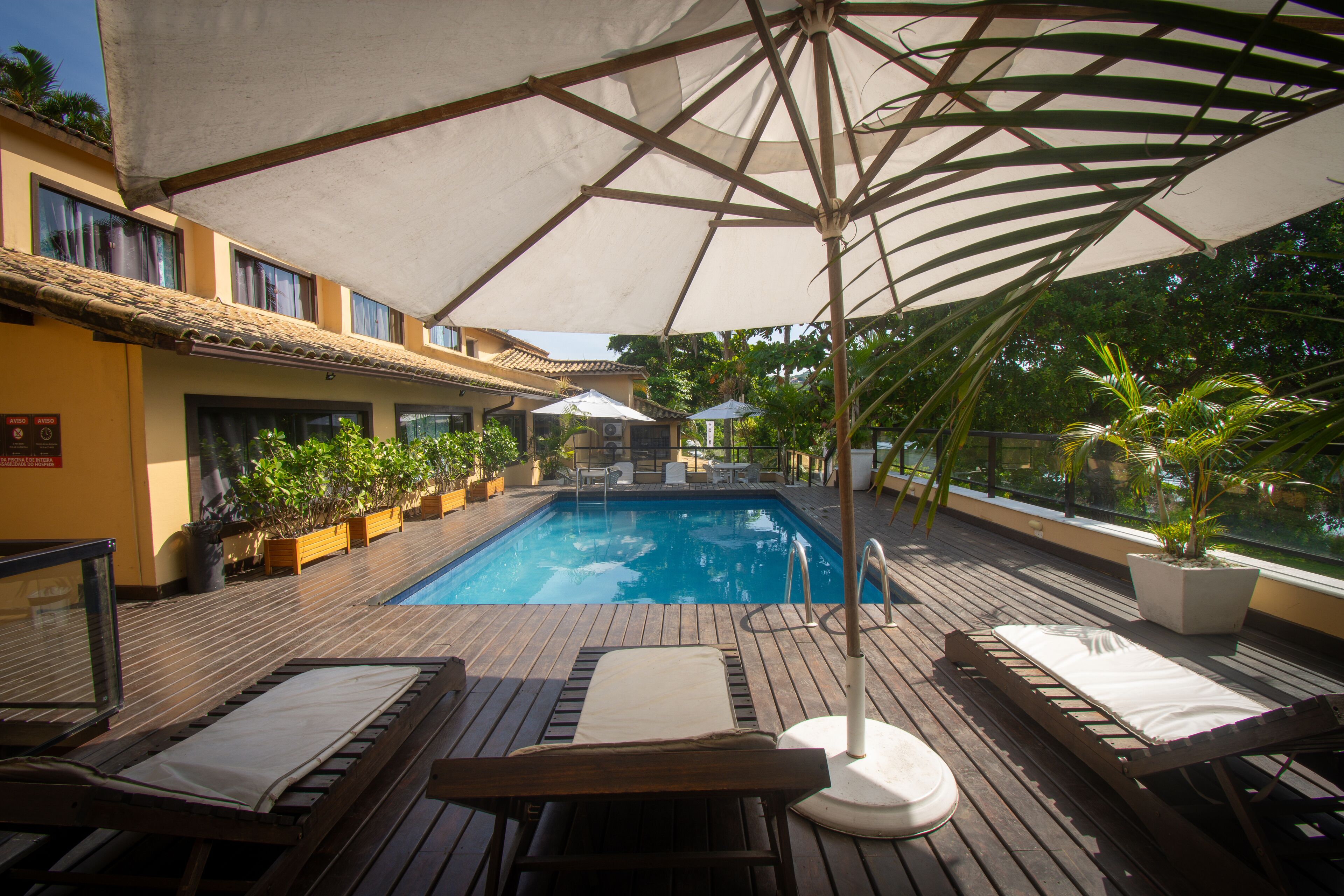 A wooden deck with a pool, lounge chairs, and umbrellas.